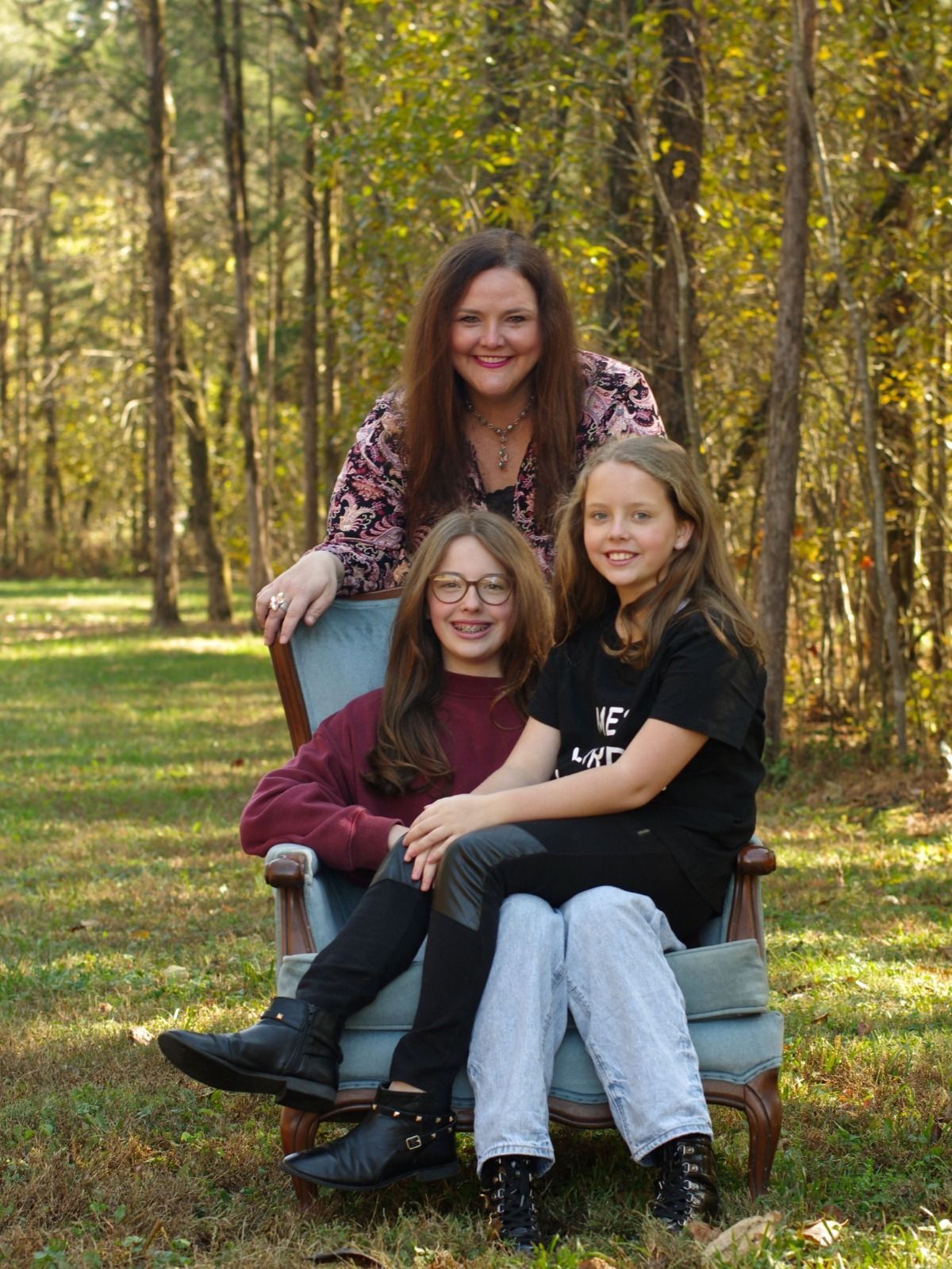 A woman and two girls are sitting in a chair in the woods.
