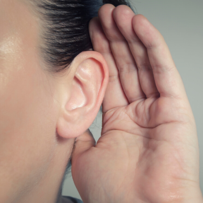 A woman is holding her hand to her ear to hear something.