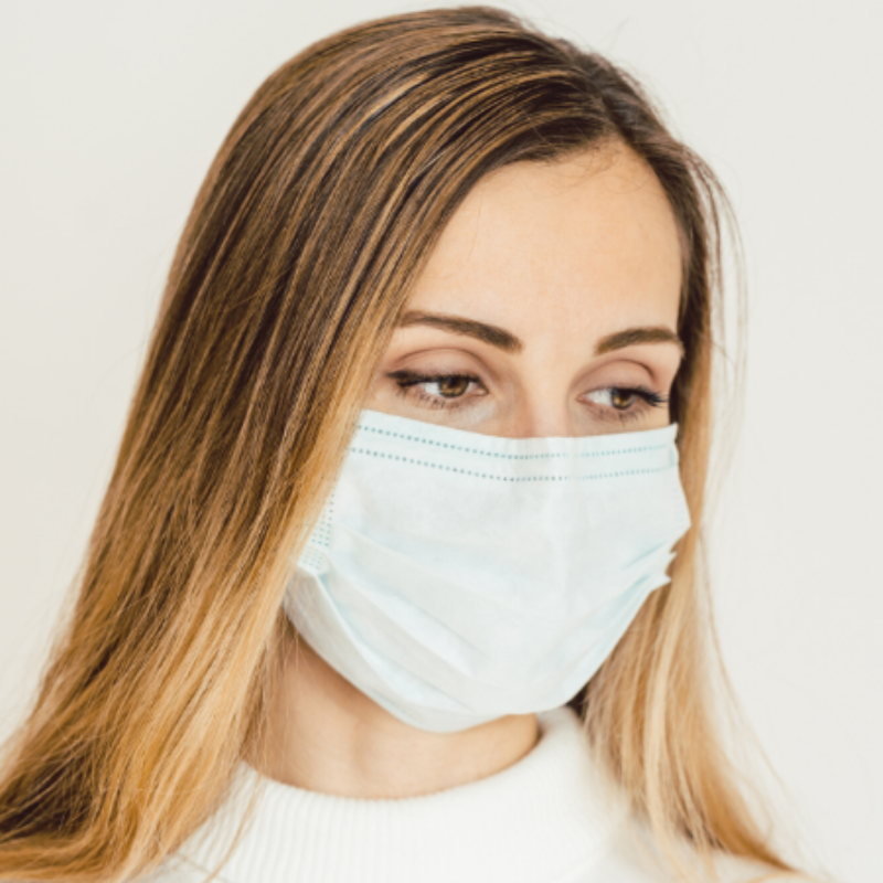 A woman wearing a white face mask with her eyes closed