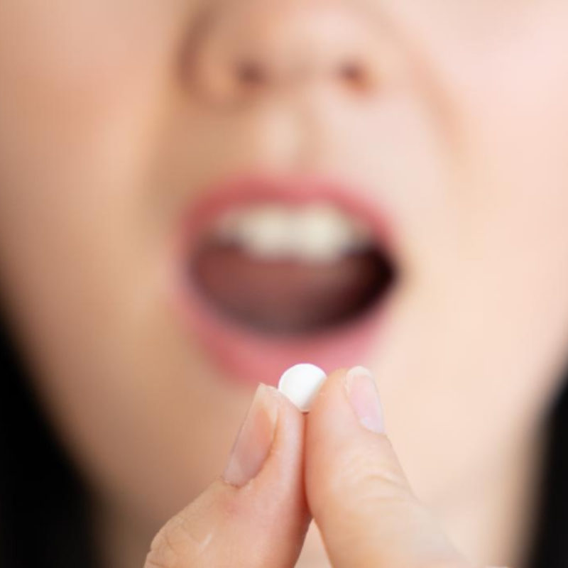 A woman is holding a small white pill in her hand in front of her mouth.