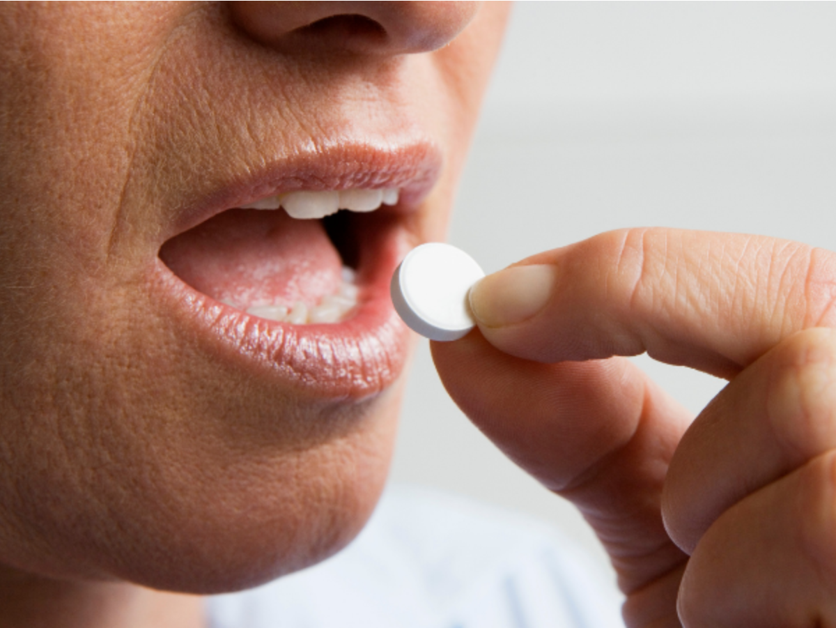 A woman is taking a pill in her mouth.