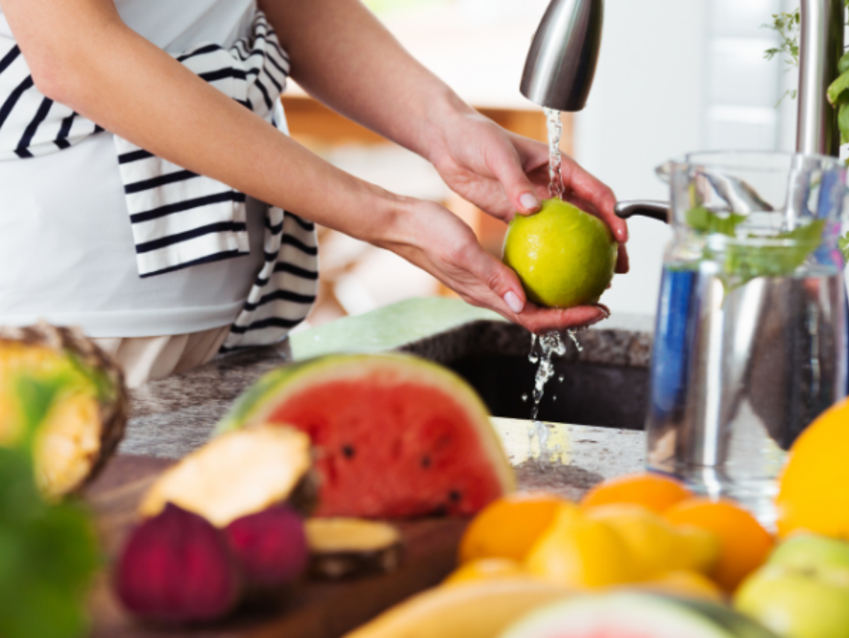 A woman is washing fruit in a kitchen sink
