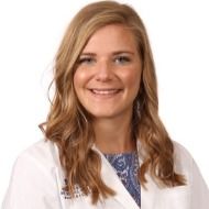A woman in a white lab coat is smiling for the camera.