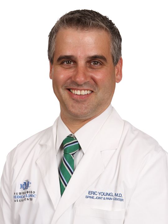 Eric young m.d. is smiling and wearing a white coat and green tie