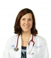 A woman in a white lab coat with a stethoscope around her neck is smiling.