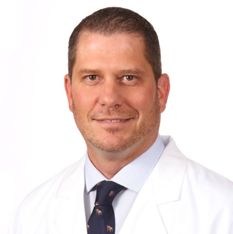 A man in a white coat and tie is smiling for the camera