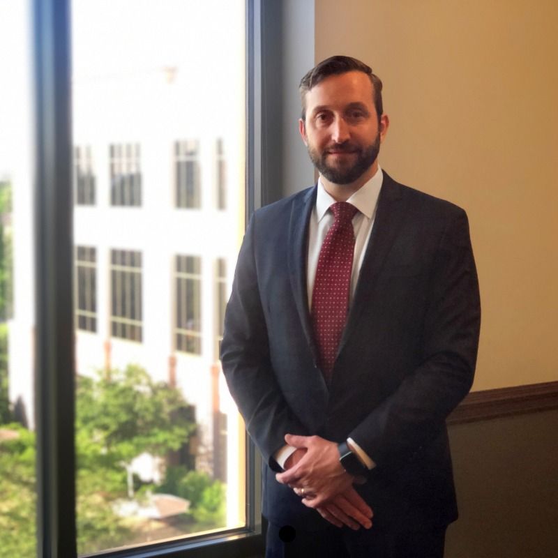 A man in a suit and tie stands in front of a window