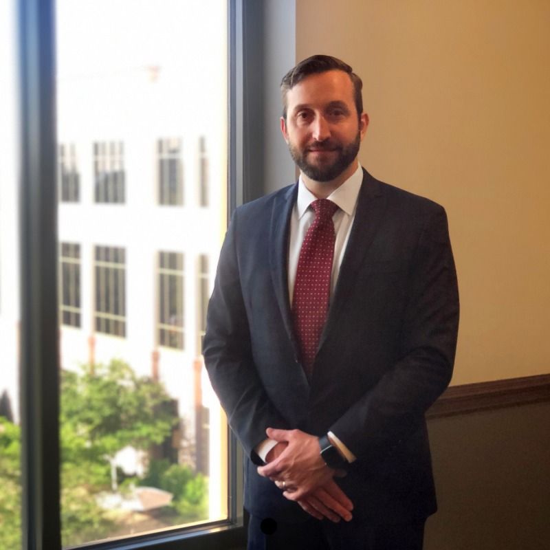 A man in a suit and tie stands in front of a window