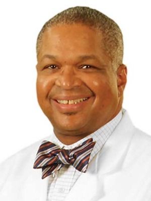 A man in a white coat and bow tie is smiling.