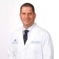 A man in a white coat and tie is standing in front of a white background.