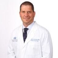 A man in a white coat and tie is standing in front of a white background.