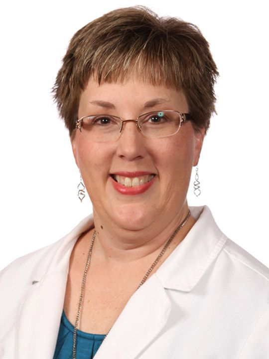 A woman wearing glasses and a white coat smiles for the camera