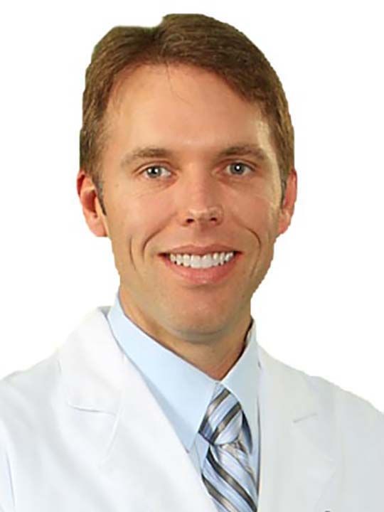 A man in a white coat and tie is smiling for the camera.