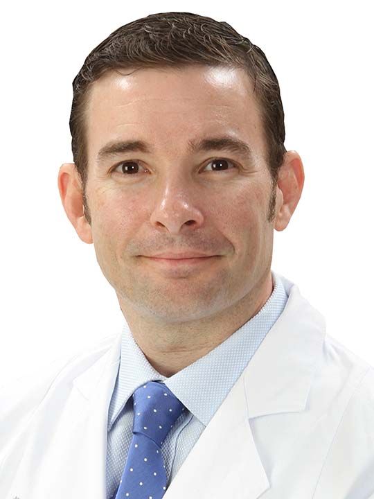A man in a white coat and blue tie is smiling