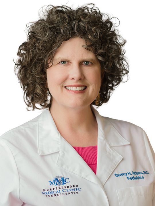 A woman with curly hair is wearing a white lab coat