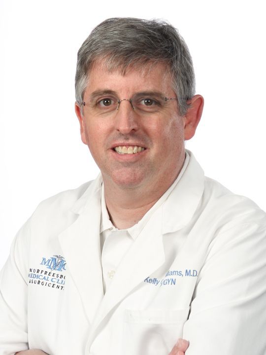 A man in a white lab coat is smiling with his arms crossed.