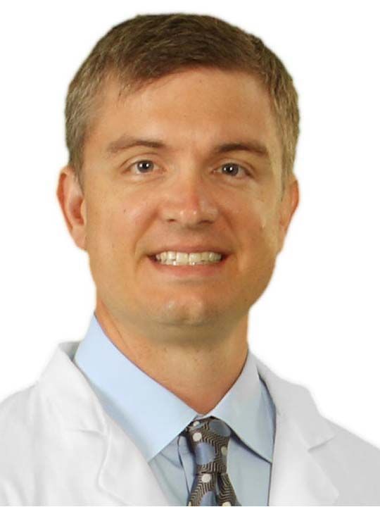 A man in a white coat and tie smiles for the camera