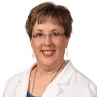 A woman wearing glasses and a white lab coat is smiling for the camera.