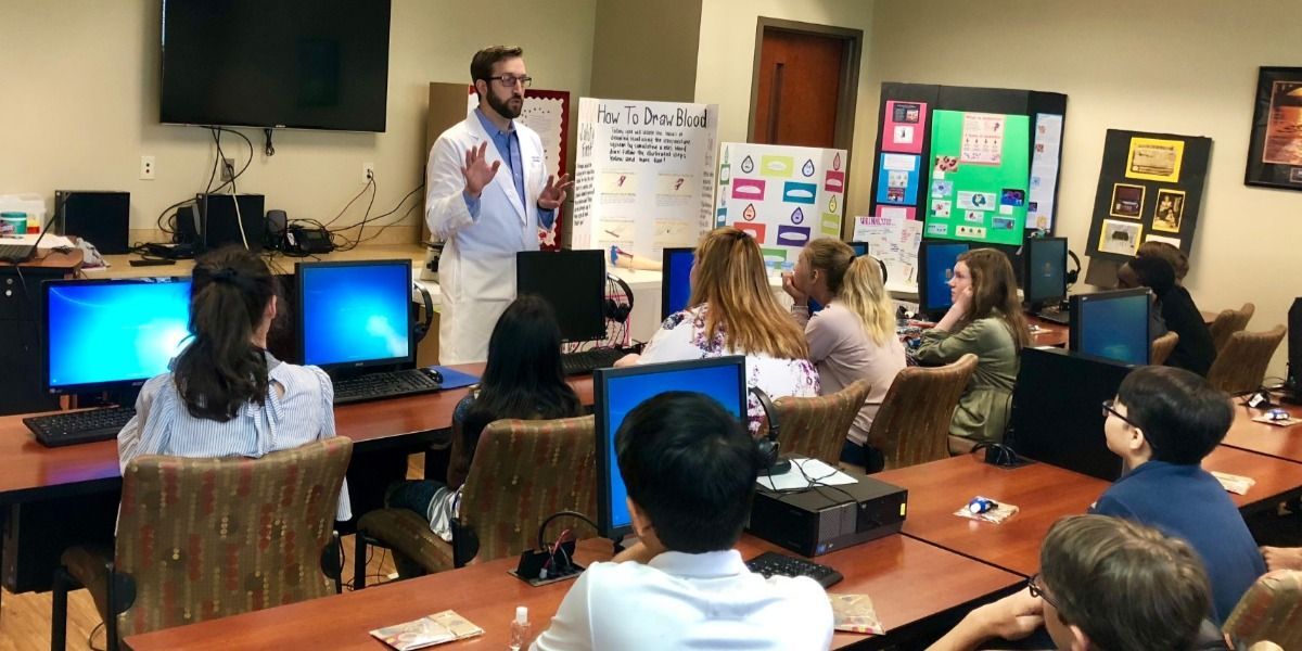 A man is giving a presentation to a group of students in a computer lab.
