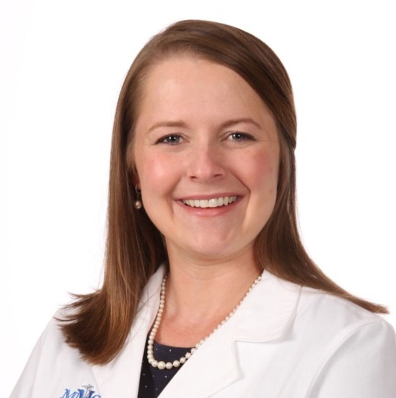 A smiling woman wearing a white lab coat and a pearl necklace