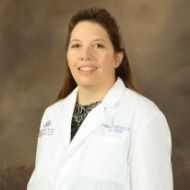 A woman in a white lab coat is smiling for the camera.