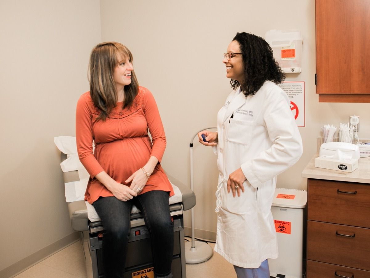 A pregnant woman is sitting in an exam room talking to a doctor.