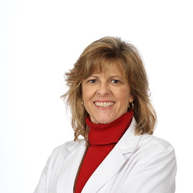 A woman wearing a white lab coat and a red turtleneck smiles for the camera