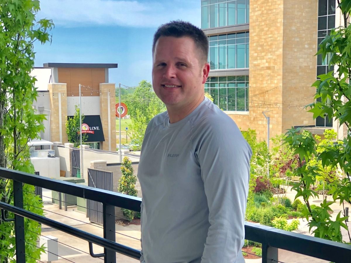 A man is standing on a balcony with a building in the background.
