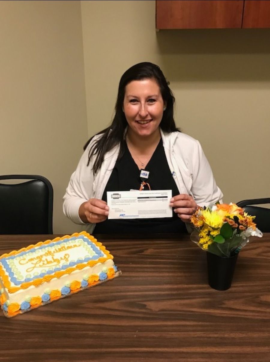 A woman is sitting at a table holding a check in front of a cake.