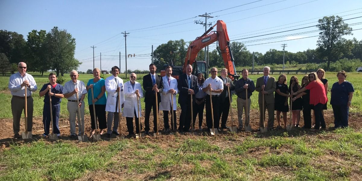 A group of people are standing in a field holding shovels.