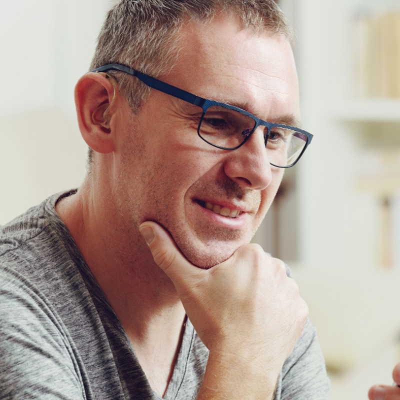 A man wearing glasses is smiling with his hand on his chin