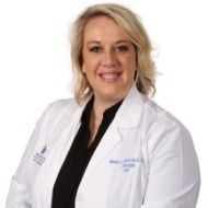 A woman in a white lab coat is smiling for the camera.