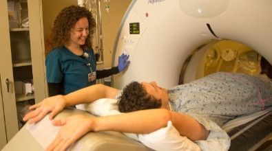 A woman is standing next to a patient laying in a ct scan machine.