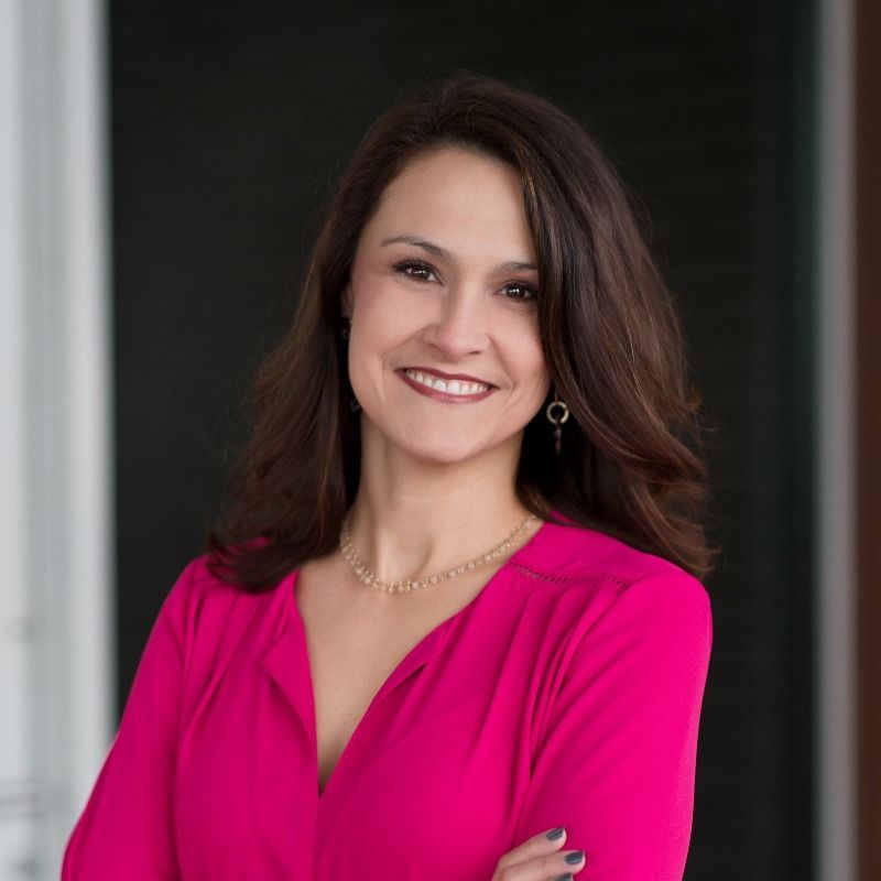 A woman in a pink shirt is smiling for the camera with her arms crossed.
