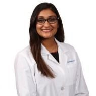 A woman in a white lab coat and glasses is smiling.