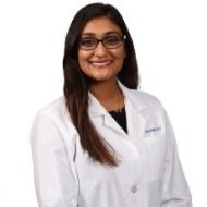 A woman in a white lab coat and glasses is smiling.