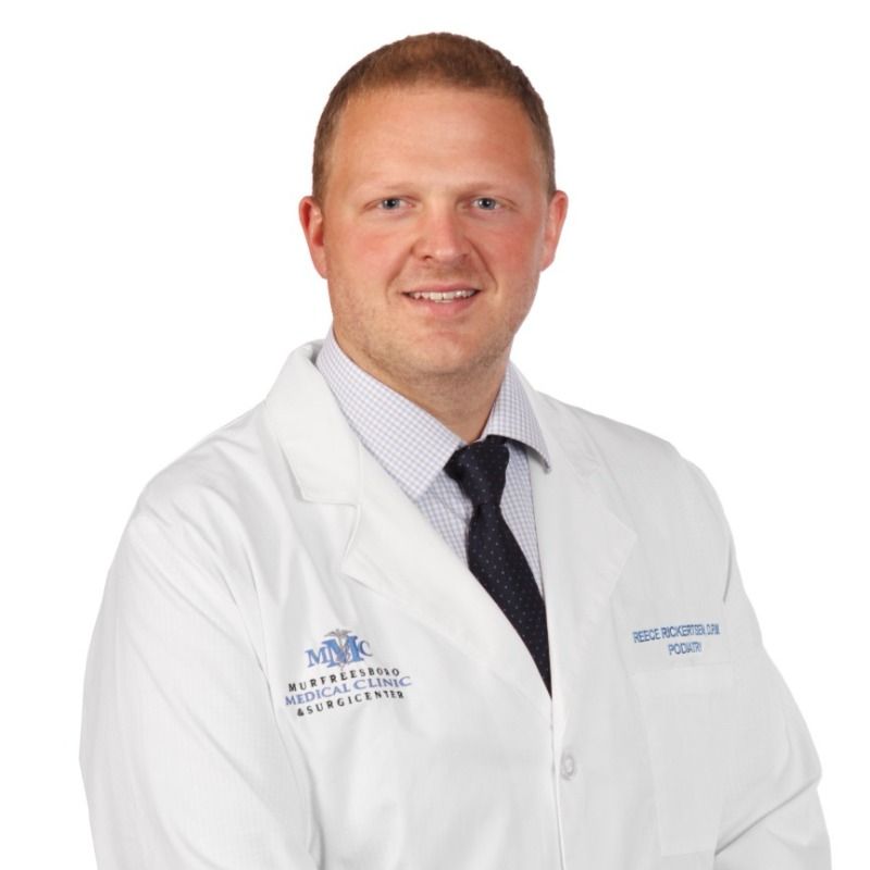 A man in a white lab coat and tie is smiling