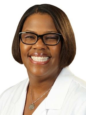 A woman wearing glasses and a white coat is smiling