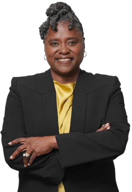 Smiling person in a black blazer and yellow top, standing with arms crossed on a white background