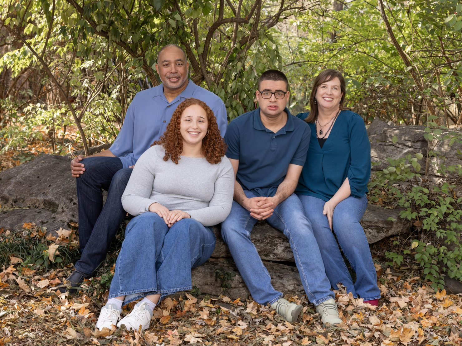 Rick with his wife and two adult children, sitting on a rock together outside. 