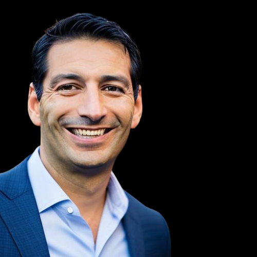 A professional headshot of a smiling person wearing a blue blazer and light blue dress shirt against a black background.