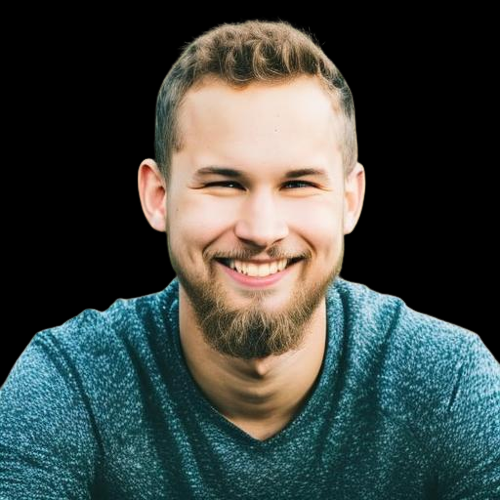 A person with a beard and short hair smiling warmly, wearing a textured teal V-neck shirt against a black background.