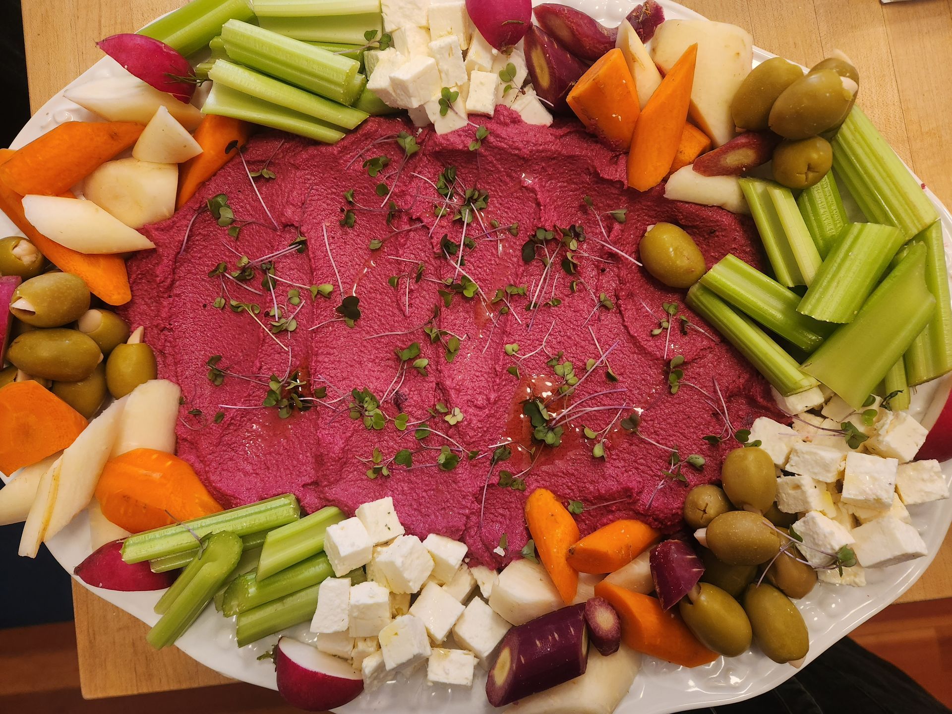 A white plate topped with vegetables and hummus on a table.