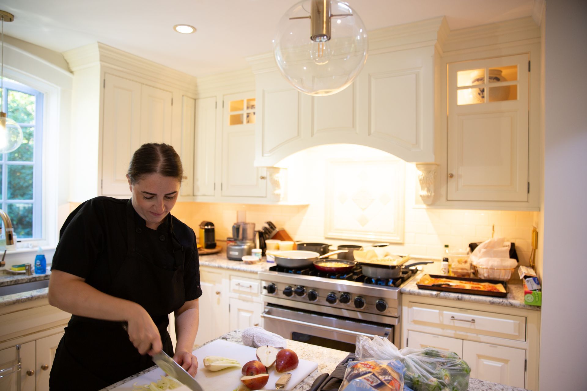 A woman is cutting vegetables on a cutting board in a kitchen.