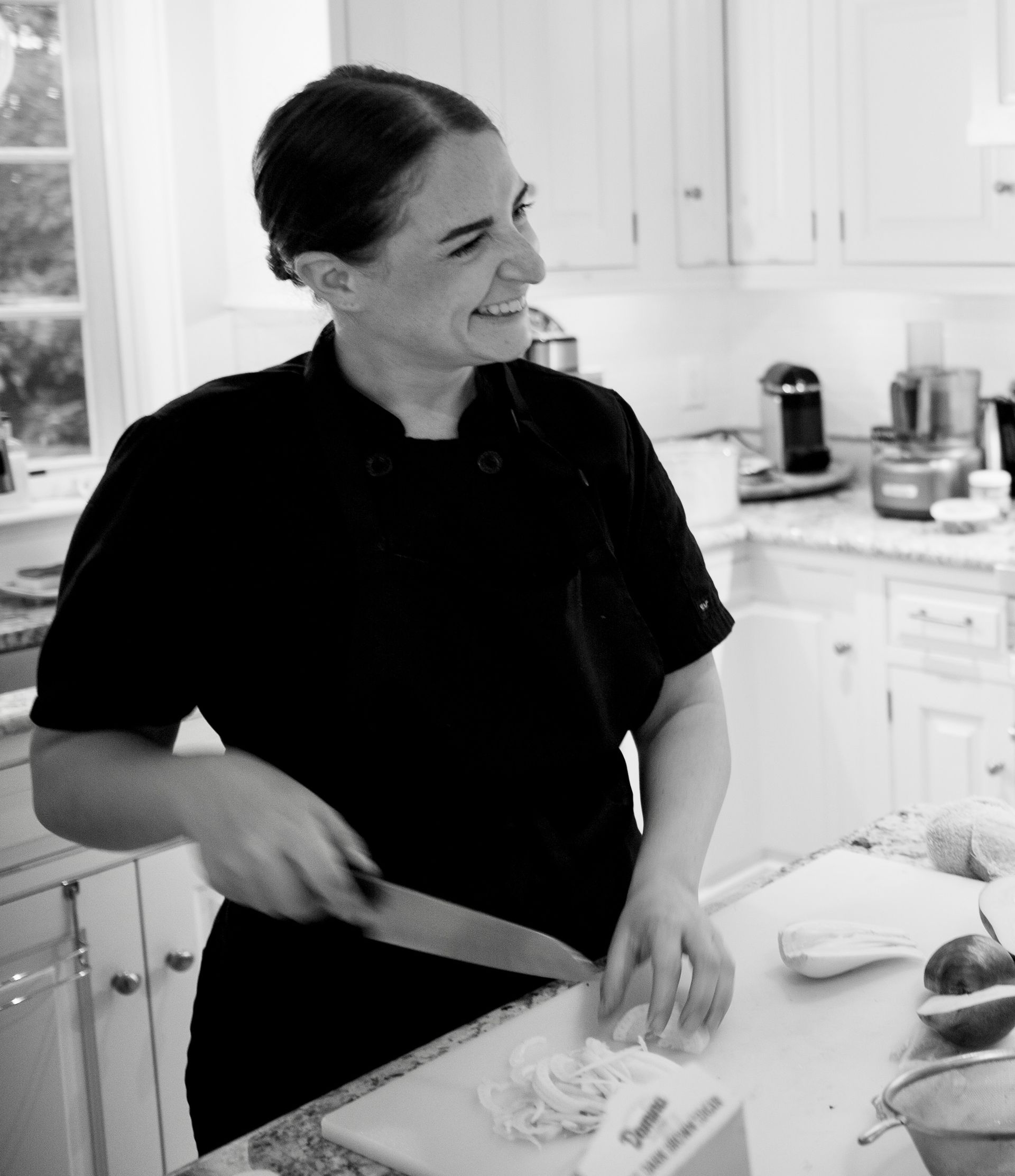 A woman is smiling while cutting vegetables in a kitchen