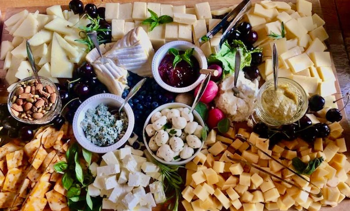 A wooden cutting board topped with a variety of cheeses , fruits and nuts.