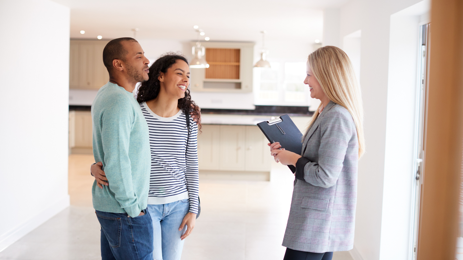 Couple viewing a new home with a realtor; looking at the kitchen; the realtor holds a clipboard.