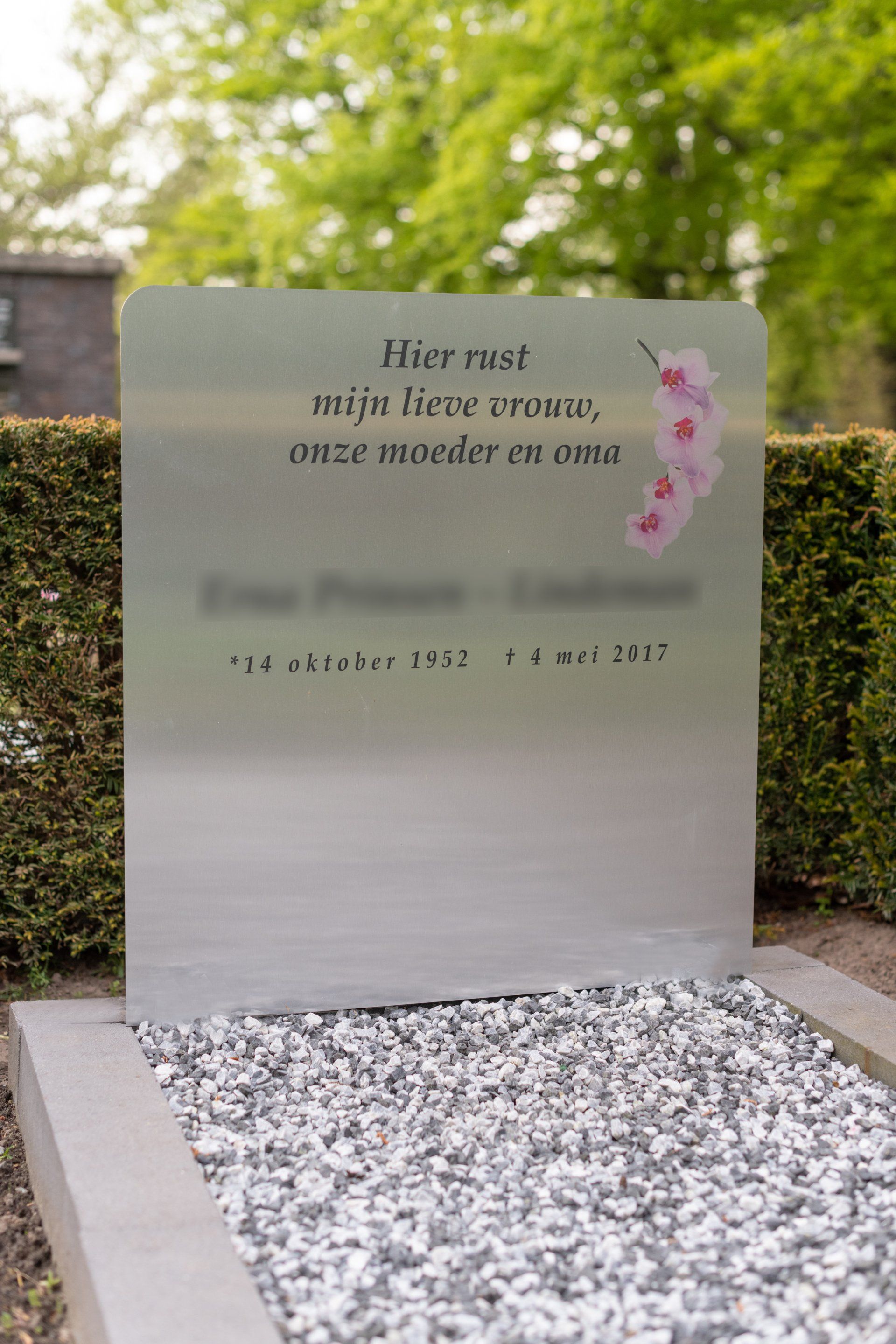 Een grafsteen van roestvrij staal met een roze bloem erop. Grafmonument.