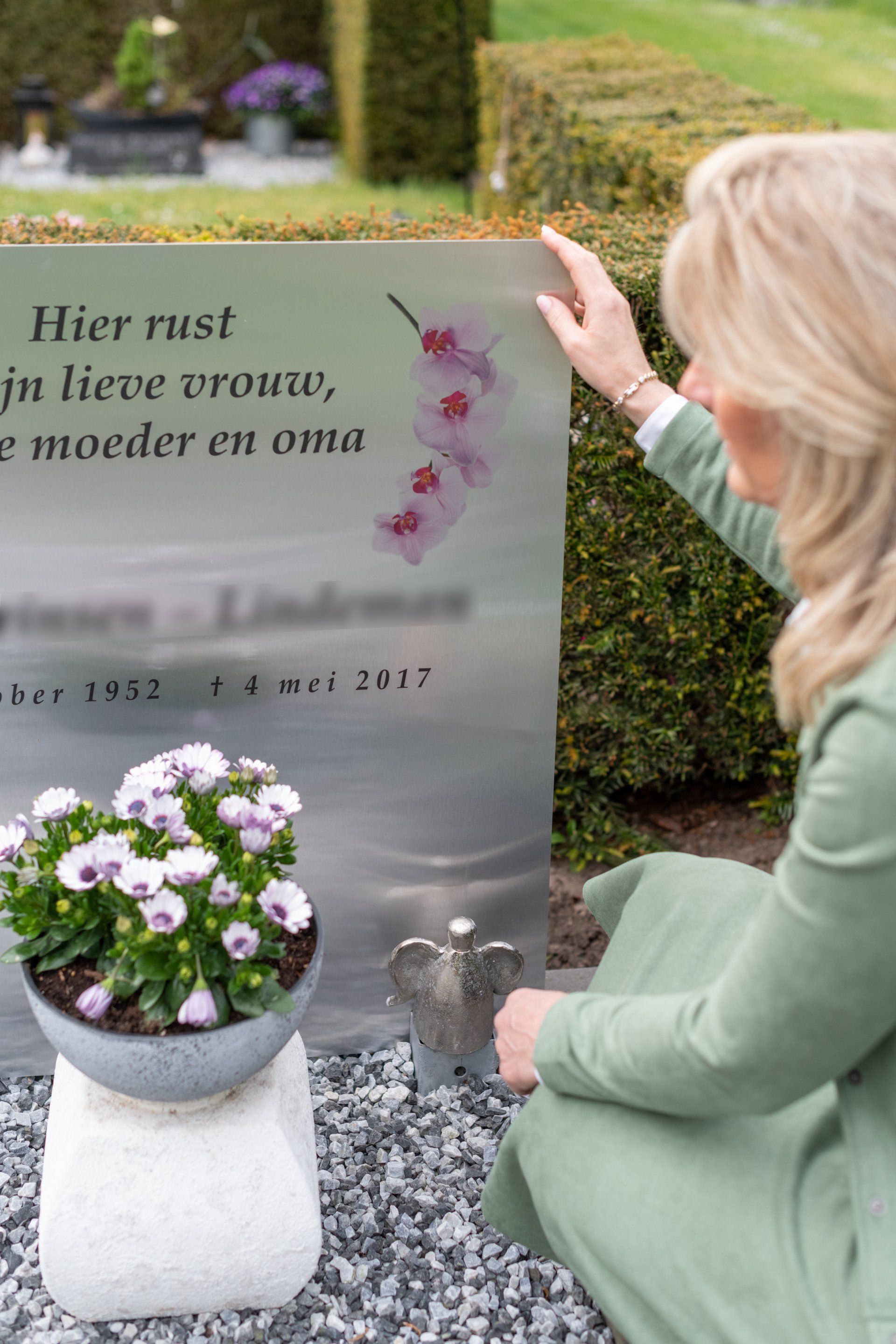 Een vrouw in een groene jurk knielt voor een graf bij een grafmonument.