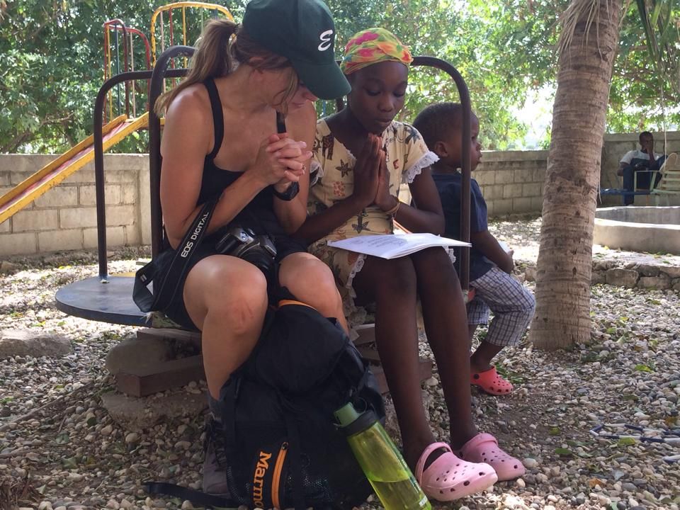 A woman wearing a green hat is sitting on a bench with two children.